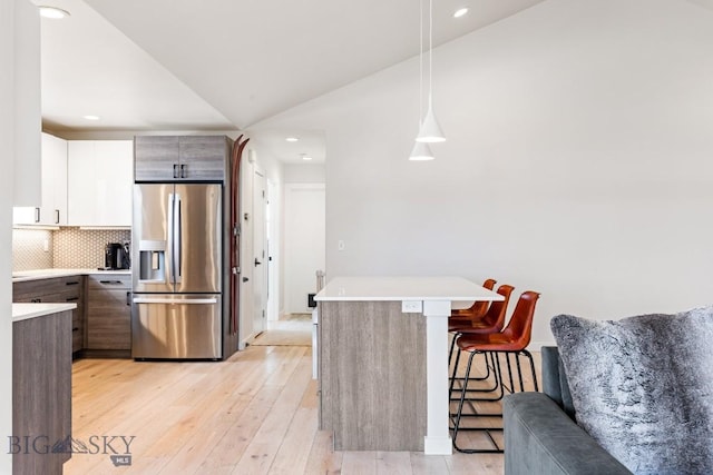 kitchen with vaulted ceiling, a breakfast bar, pendant lighting, white cabinetry, and stainless steel fridge with ice dispenser