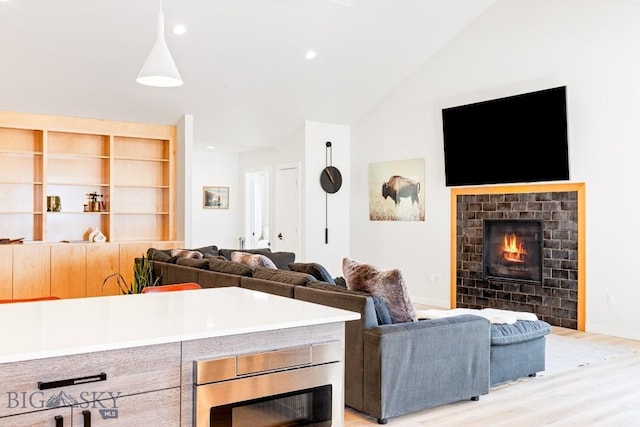 living room with lofted ceiling, a brick fireplace, and light hardwood / wood-style flooring