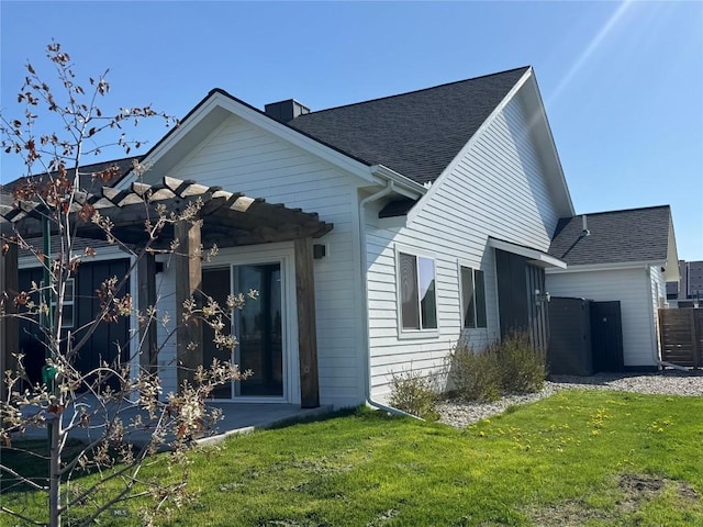 rear view of property with roof with shingles, a chimney, and a lawn