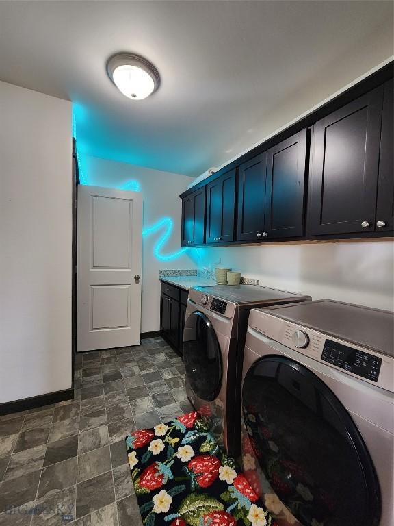 washroom featuring baseboards, cabinet space, stone finish floor, and washing machine and clothes dryer