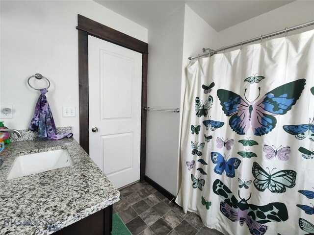 full bath with a shower with shower curtain, vanity, stone finish flooring, and baseboards