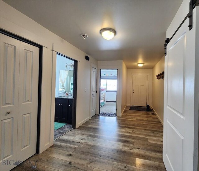 corridor with baseboards, a barn door, and wood finished floors