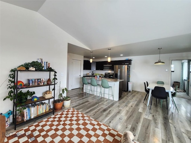 kitchen with high vaulted ceiling, a center island, stainless steel appliances, light hardwood / wood-style floors, and a kitchen bar