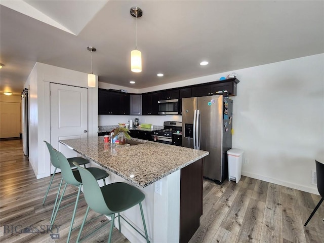 kitchen with light stone counters, light wood-type flooring, appliances with stainless steel finishes, and a sink