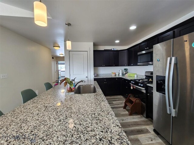 kitchen featuring a sink, light stone counters, appliances with stainless steel finishes, and dark cabinetry