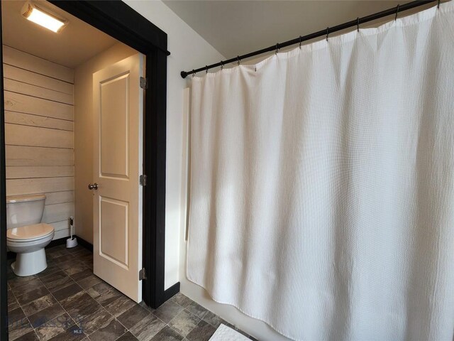 bathroom featuring wood walls, toilet, a shower with shower curtain, and stone finish floor