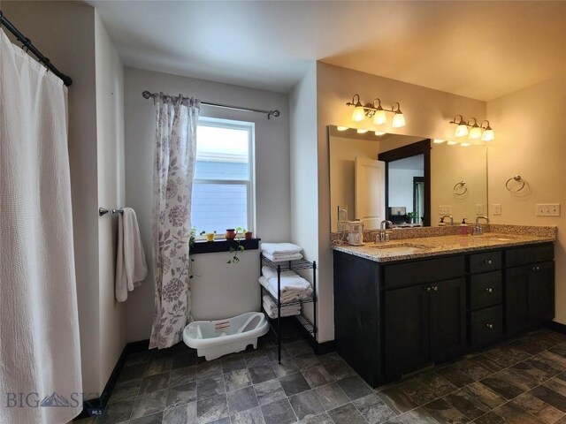 bathroom featuring double vanity, stone finish floor, baseboards, and a sink