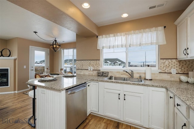 kitchen featuring white cabinetry, sink, stainless steel dishwasher, light stone counters, and kitchen peninsula