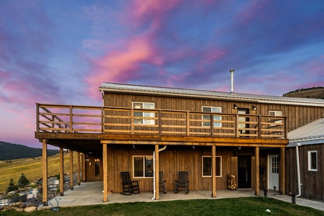 back house at dusk with a wooden deck, a yard, and a patio