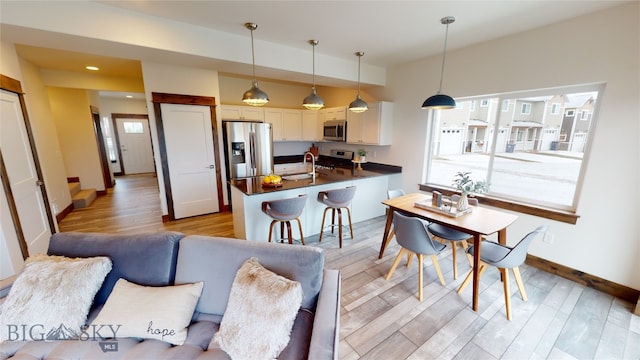 kitchen with white cabinetry, a kitchen breakfast bar, hanging light fixtures, light hardwood / wood-style floors, and stainless steel appliances