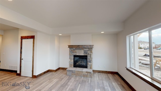 unfurnished living room with a stone fireplace and light hardwood / wood-style floors