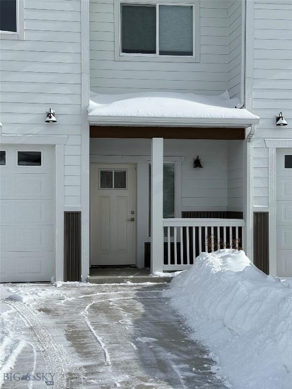 snow covered property entrance with a garage and covered porch