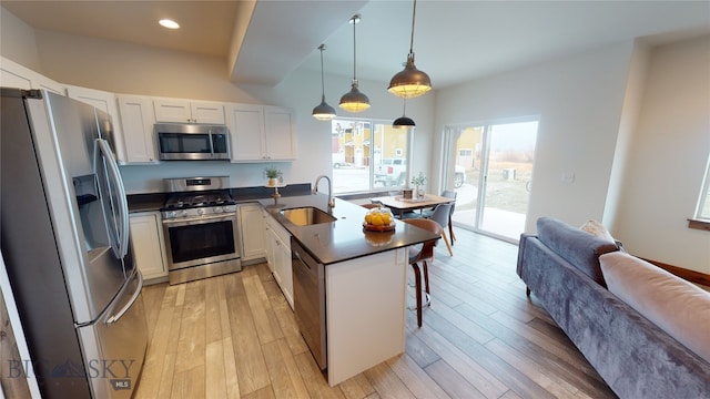 kitchen featuring sink, stainless steel appliances, white cabinets, a kitchen bar, and decorative light fixtures