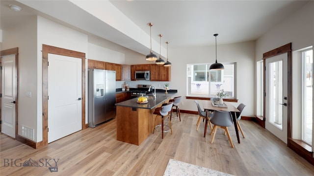 kitchen featuring decorative light fixtures, stainless steel appliances, light hardwood / wood-style floors, and a kitchen breakfast bar