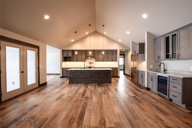 kitchen with beverage cooler, dark wood finished floors, lofted ceiling, an island with sink, and high quality fridge