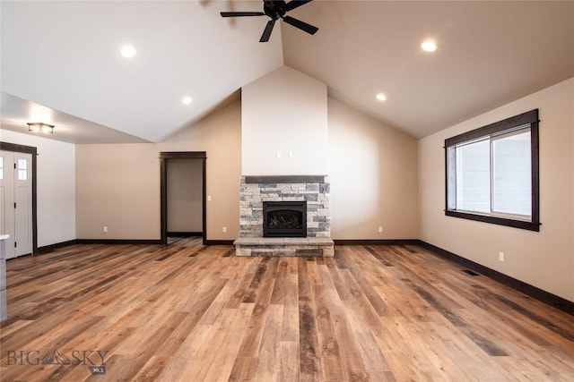 unfurnished living room with wood finished floors, baseboards, lofted ceiling, ceiling fan, and a stone fireplace