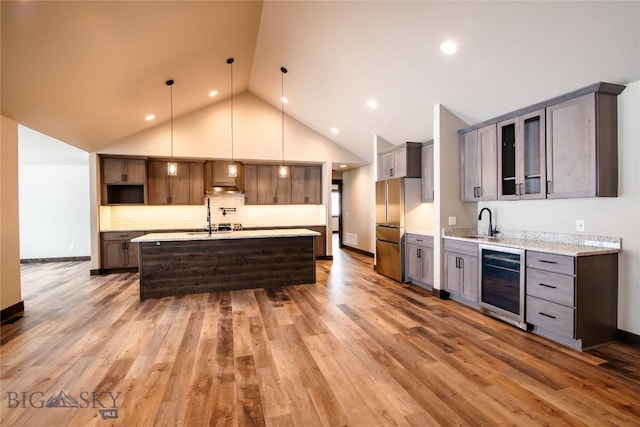 kitchen with beverage cooler, a center island with sink, a sink, wood finished floors, and freestanding refrigerator