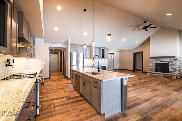 kitchen with light stone counters, a sink, glass insert cabinets, appliances with stainless steel finishes, and wall chimney range hood