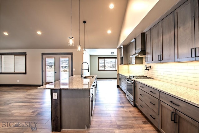 kitchen with a kitchen island with sink, a sink, wall chimney exhaust hood, stainless steel range with gas stovetop, and vaulted ceiling