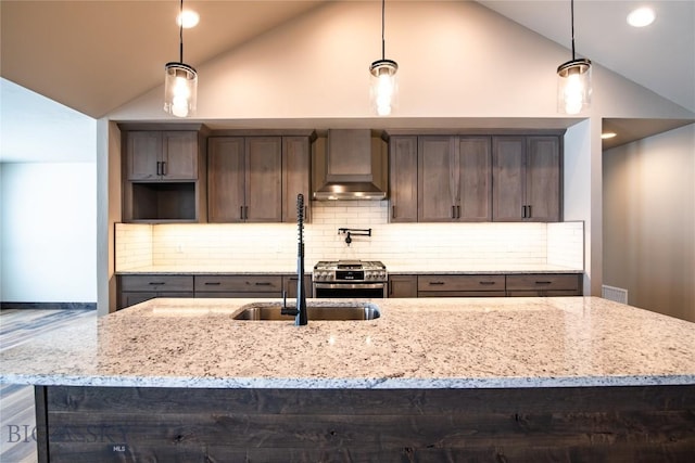 kitchen featuring vaulted ceiling, wall chimney range hood, light stone countertops, and stainless steel gas stove