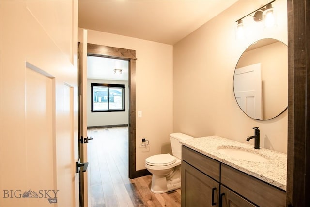 half bath featuring baseboards, toilet, wood finished floors, and vanity