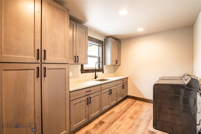 washroom with baseboards, washing machine and clothes dryer, cabinet space, a sink, and light wood-type flooring