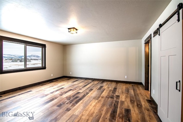 unfurnished room with a textured ceiling, baseboards, a barn door, and wood finished floors