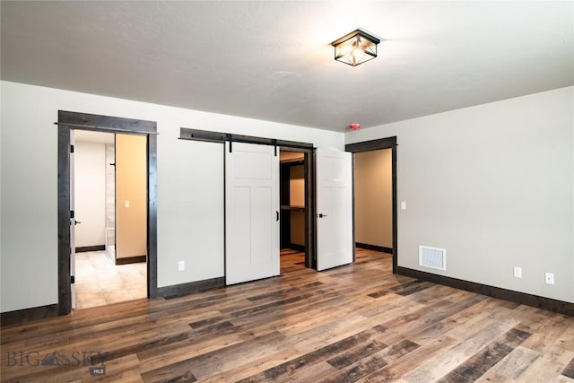 unfurnished bedroom featuring a barn door, wood finished floors, visible vents, and baseboards