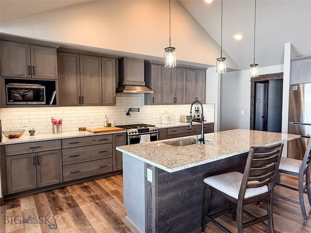 kitchen with stainless steel appliances, a sink, dark wood-type flooring, pendant lighting, and wall chimney exhaust hood