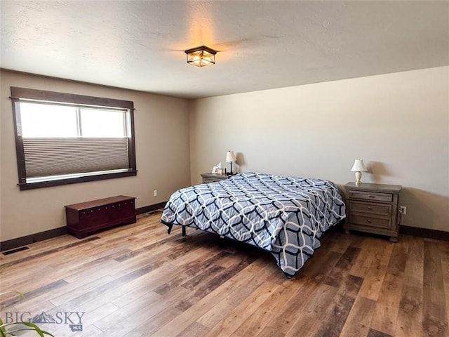 bedroom with visible vents, baseboards, a textured ceiling, and wood finished floors