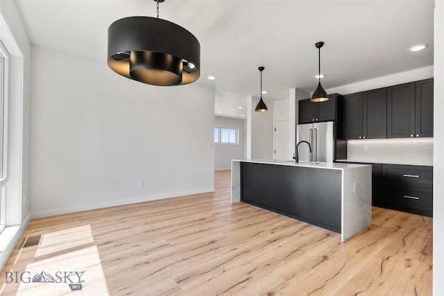 kitchen featuring hanging light fixtures, an island with sink, high end fridge, and light hardwood / wood-style flooring