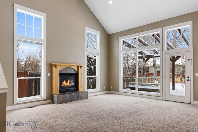 unfurnished living room with a healthy amount of sunlight, carpet flooring, and high vaulted ceiling