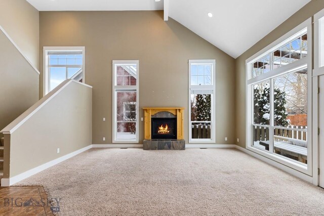 unfurnished living room with a tiled fireplace, a healthy amount of sunlight, high vaulted ceiling, and carpet flooring