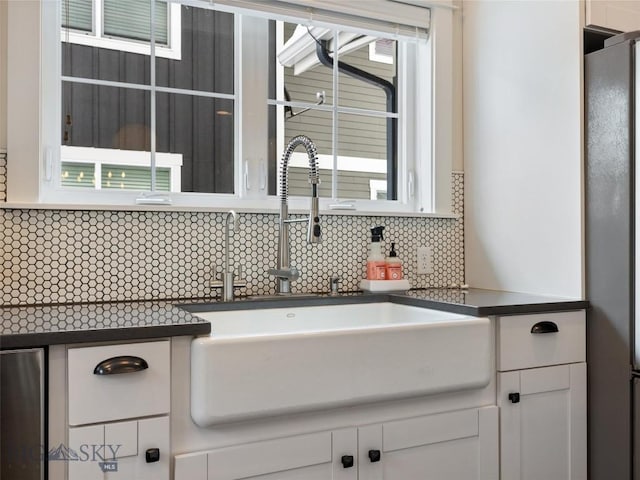 kitchen with white cabinetry, sink, backsplash, and stainless steel refrigerator