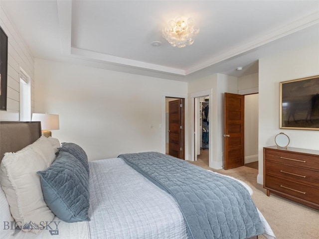 bedroom with a raised ceiling, a walk in closet, light colored carpet, and a closet