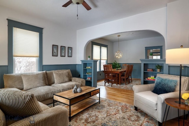 living room with ceiling fan with notable chandelier, light wood-type flooring, and a wealth of natural light