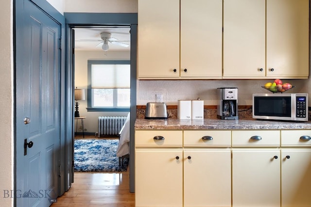 kitchen featuring cream cabinets, radiator, ceiling fan, and light hardwood / wood-style flooring