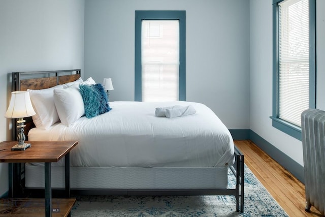 bedroom featuring multiple windows, wood-type flooring, and radiator heating unit