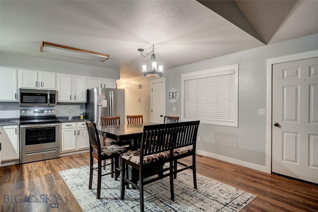 dining room with dark wood-type flooring, a textured ceiling, and a notable chandelier