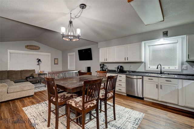 dining area featuring sink, light hardwood / wood-style flooring, an inviting chandelier, a textured ceiling, and vaulted ceiling