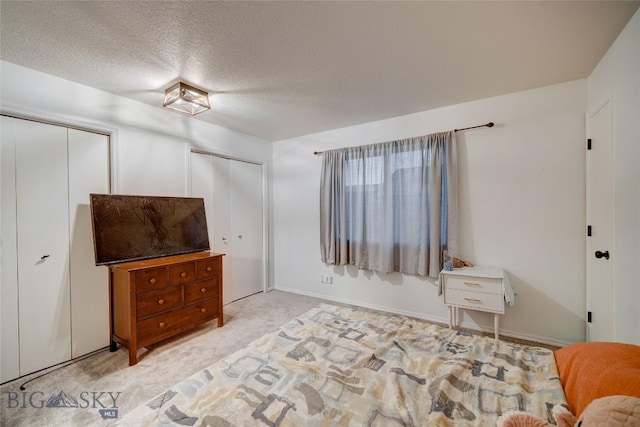 bedroom with a textured ceiling, light carpet, and two closets