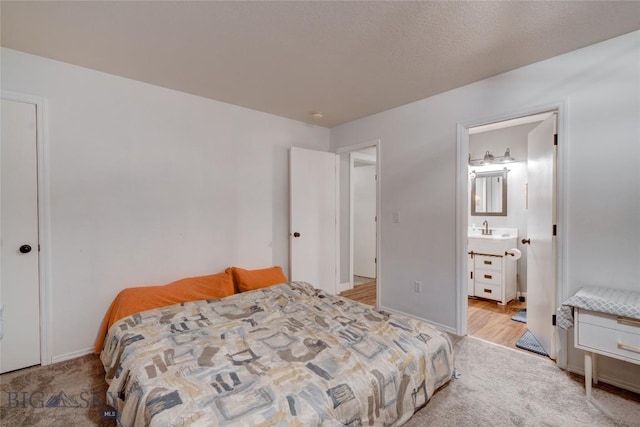 bedroom with light carpet, connected bathroom, sink, and a textured ceiling