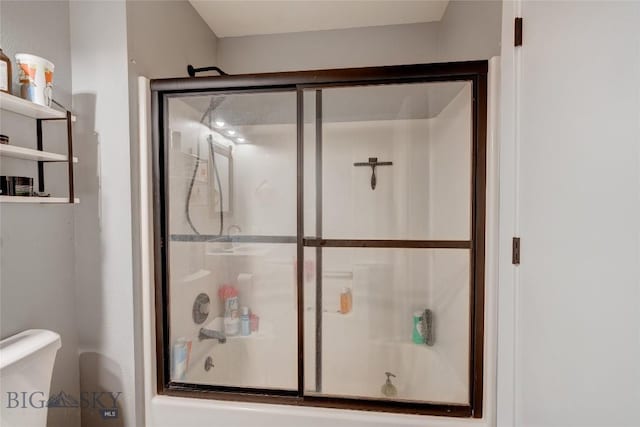 bathroom featuring toilet and shower / bath combination with glass door