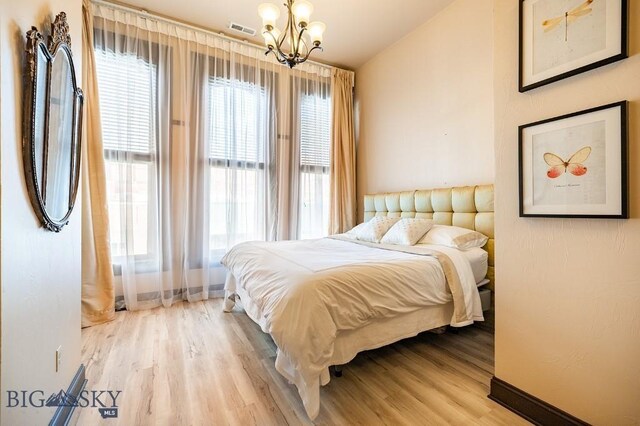 bedroom featuring an inviting chandelier, vaulted ceiling, and light hardwood / wood-style floors