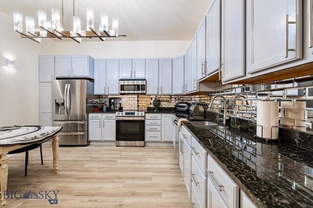 kitchen with pendant lighting, sink, dark stone countertops, stainless steel appliances, and decorative backsplash