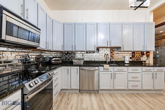 kitchen featuring white cabinetry, stainless steel appliances, sink, and dark stone countertops