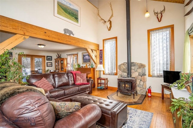 living room with french doors, a towering ceiling, a wood stove, and light hardwood / wood-style flooring