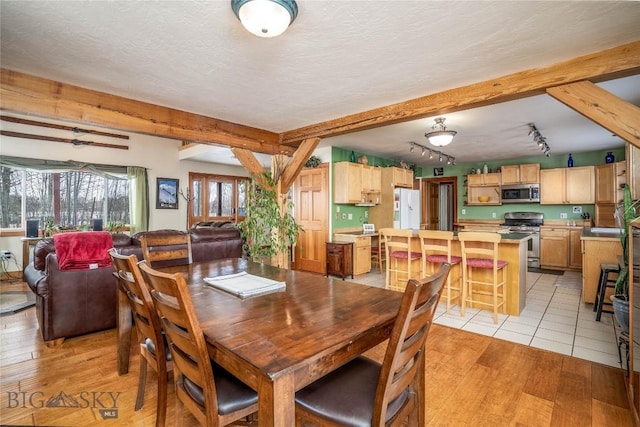 dining area featuring a textured ceiling, light hardwood / wood-style floors, and beamed ceiling