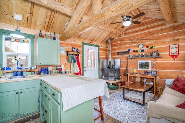 kitchen with green cabinetry, lofted ceiling with beams, wooden ceiling, a wood stove, and wooden walls