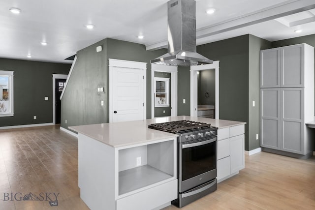 kitchen with white cabinetry, island exhaust hood, stainless steel range with gas stovetop, a kitchen island, and light wood-type flooring